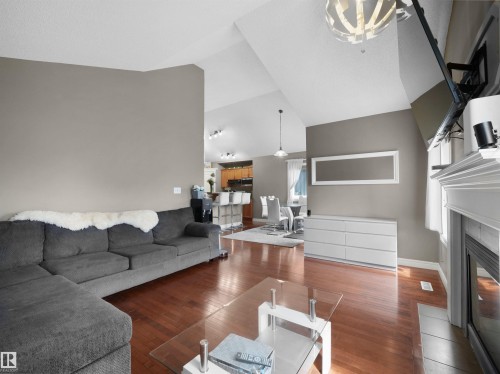 Spacious living area featuring vaulted ceilings, wood-finish flooring, a white mantel fireplace, and a contemporary overhead light fixture - 4021 158 Avenue Nw, Edmonton, AB - Indoor Photo Showing Living Room With Fireplace