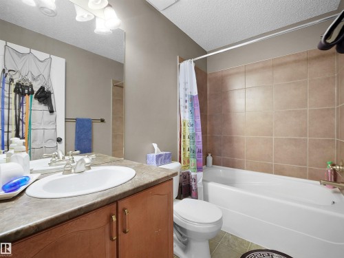 Full bathroom with a white tub and shower combination, tan tiled shower surround, wood-finish vanity with an integrated sink, and a large wall-mounted mirror - 4021 158 Avenue Nw, Edmonton, AB - Indoor Photo Showing Bathroom
