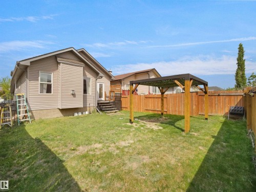 Spacious backyard featuring a wooden privacy fence, a contemporary wood pergola with a dark-finished top, a grassy area, and a rear exterior with a deck and steps - 4021 158 Avenue Nw, Edmonton, AB - Outdoor