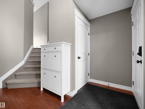 Entryway featuring warm wood-finish flooring, staircase with carpeted treads, and painted paneled doors with black hardware - 4021 158 Avenue Nw, Edmonton, AB - Indoor Photo Showing Other Room