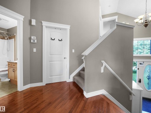 Rich wood-finish flooring extending from the entryway, white interior doors with decorative trim, a staircase with carpeted treads and white handrails, and a bathroom entrance with a wood vanity - 4021 158 Avenue Nw, Edmonton, AB - Indoor Photo Showing Other Room