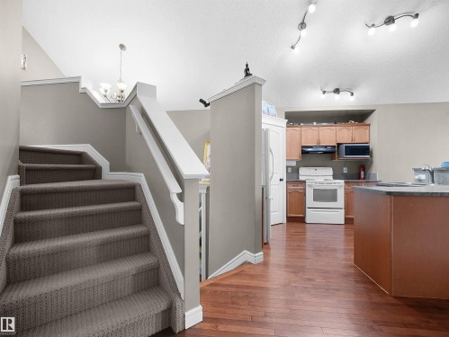 Carpeted staircase with white railings, hardwood flooring, and kitchen featuring light wood cabinetry, white appliances, and a dark countertop - 4021 158 Avenue Nw, Edmonton, AB - Indoor Photo Showing Kitchen