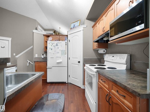 Kitchen featuring wood-finish flooring, light wood cabinetry, stone-look countertops, and a stainless steel over-the-range microwave - 4021 158 Avenue Nw, Edmonton, AB - Indoor Photo Showing Kitchen