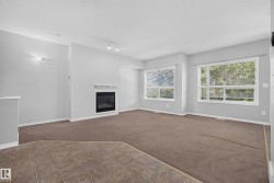 Living area featuring a built-in fireplace with a white mantel, two large windows, brown carpeting, and a tiled entry - 