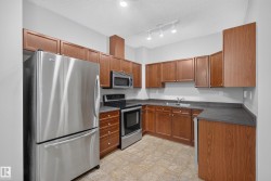 U-shaped kitchen featuring wood-finish cabinetry, dark countertops, and stainless steel appliances including a refrigerator, range, and microwave - 