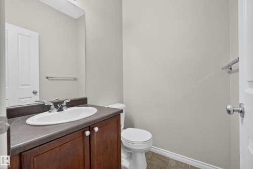 Bathroom featuring a wood-finish vanity with an integrated sink and dark countertop, chrome fixtures, and tiled flooring - #113 3010 33 Av Nw, Edmonton, AB 