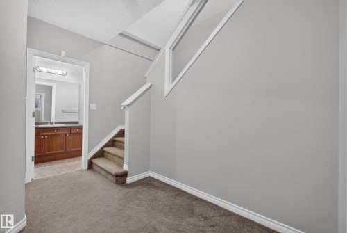 Carpeted hallway with light gray walls, white trim, and a carpeted staircase featuring a white handrail - #113 3010 33 Av Nw, Edmonton, AB 