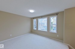 Spacious room featuring light beige wall paint, plush light-colored carpeting, a contemporary flush-mount ceiling light, and multiple large windows with white trim and a dark curtain rod - 