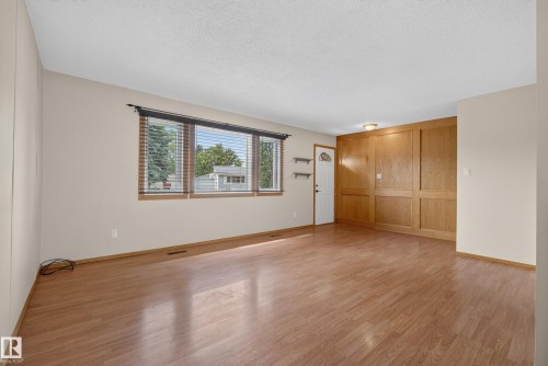 Spacious room featuring wood-finish flooring, a multi-pane window with horizontal blinds, and paneled wood wall accents - 3 Bristow Crescent, Spruce Grove, AB - Indoor