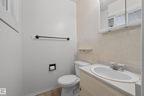 Bathroom featuring a single vanity with an integrated sink, a mirrored medicine cabinet, a toilet, a black metal towel bar, and neutral floor tiling - 3 Bristow Crescent, Spruce Grove, AB - Indoor Photo Showing Bathroom