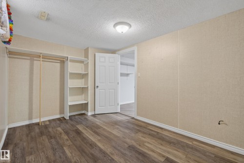 Room featuring wood-finish flooring, light-colored wall panels, white trim, and a white six-panel door - 3 Bristow Crescent, Spruce Grove, AB - Indoor Photo Showing Other Room
