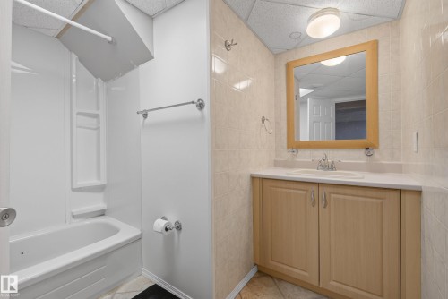 Bathroom featuring a light-toned vanity with a white countertop and integrated sink, a large framed mirror, a tub/shower combination with a white surround, and tiled walls and flooring - 3 Bristow Crescent, Spruce Grove, AB - Indoor Photo Showing Bathroom