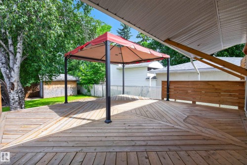 Expansive wood-finish deck with a built-in privacy wall, featuring a covered pergola area and surrounding mature trees - 3 Bristow Crescent, Spruce Grove, AB - Outdoor With Deck Patio Veranda With Exterior