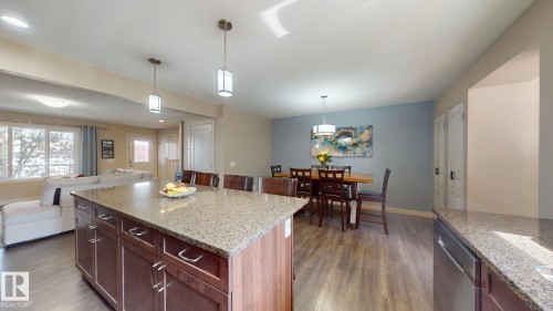 Kitchen island with granite countertop, dark wood-finish cabinetry, and pendant lighting - 6824 Evans Wynd Nw, Edmonton, AB - Indoor Photo Showing Kitchen