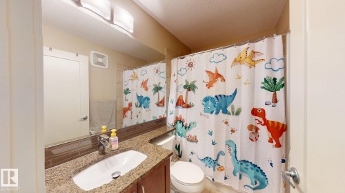 Bathroom featuring a single vanity with a granite-style countertop, undermount sink, and a tiled backsplash - 6824 Evans Wynd Nw, Edmonton, AB - Indoor Photo Showing Bathroom