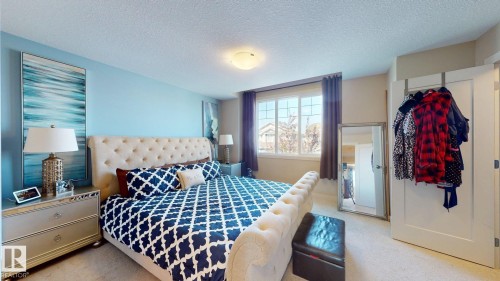 Carpeted bedroom featuring a large window with curtain rods, a light-colored ceiling, and a white door - 6824 Evans Wynd Nw, Edmonton, AB - Indoor Photo Showing Bedroom