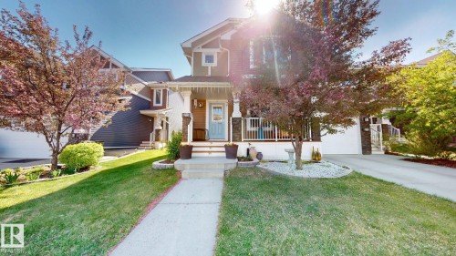 Front exterior featuring a covered porch with white railing, stone column accents, and a light blue front door - 6824 Evans Wynd Nw, Edmonton, AB - Outdoor With Facade