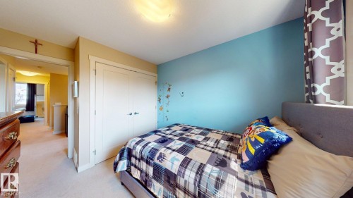 Carpeted bedroom featuring a double-door closet, a single window with patterned drapes, a light blue accent wall, and a ceiling-mounted light fixture - 6824 Evans Wynd Nw, Edmonton, AB 