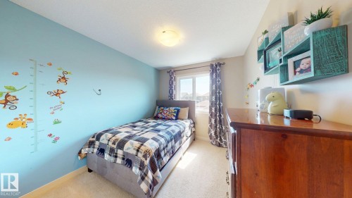 Carpeted room featuring a single window with curtains, recessed ceiling light, and a built-in wooden dresser with wall-mounted shelving - 6824 Evans Wynd Nw, Edmonton, AB 