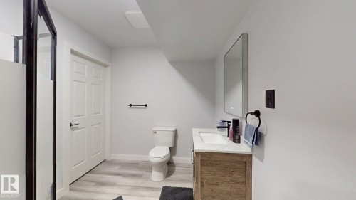 Bathroom featuring a wood-finish vanity with a white countertop and integrated sink, a rectangular mirrored medicine cabinet, and light-tone wood-finish flooring - 6824 Evans Wynd Nw, Edmonton, AB - Indoor Photo Showing Bathroom