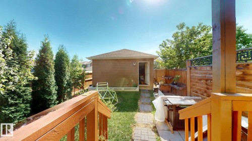 Backyard featuring a wooden privacy fence, mature evergreen trees, a detached shed with horizontal siding, a stone pathway, and a wooden deck with railing - 6824 Evans Wynd Nw, Edmonton, AB - Outdoor