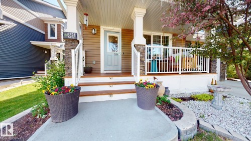 Inviting front porch featuring wood-finish decking, white railings, and stone-clad columns - 6824 Evans Wynd Nw, Edmonton, AB - Outdoor With Deck Patio Veranda