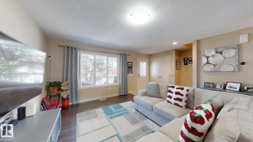 Living area featuring wood-finish flooring, a large window with drapes, and a flush mount ceiling light - 6824 Evans Wynd Nw, Edmonton, AB - Indoor Photo Showing Living Room