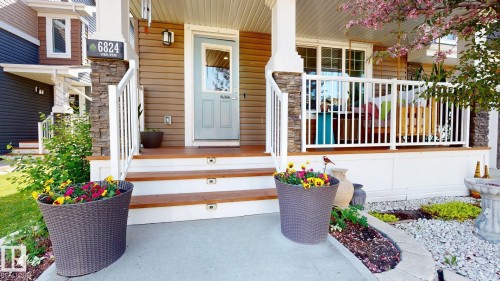 Front porch with wood-finish flooring, white railings, and stone-wrapped pillars - 6824 Evans Wynd Nw, Edmonton, AB - Outdoor With Exterior