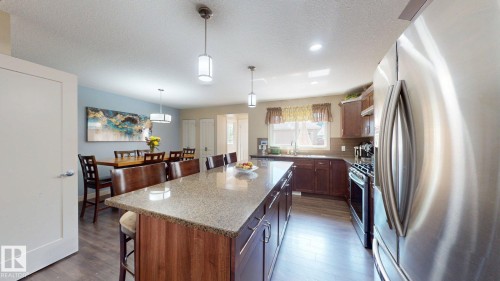 Kitchen featuring a large island with integrated seating, stainless steel appliances, dark wood cabinetry, and a light-toned countertop - 6824 Evans Wynd Nw, Edmonton, AB - Indoor Photo Showing Kitchen