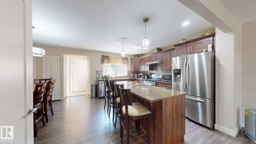 Open-concept kitchen with wood-finish flooring, a central island featuring a stone countertop, and stainless steel appliances - 6824 Evans Wynd Nw, Edmonton, AB - Indoor