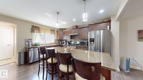 Kitchen featuring a large island with stone-finish countertops, wood-finish flooring, stainless steel appliances, recessed lighting, and wood cabinetry - 6824 Evans Wynd Nw, Edmonton, AB - Indoor Photo Showing Kitchen