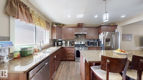 Kitchen featuring wood-finish cabinetry, stainless steel appliances, granite countertops, and wood-finish flooring - 6824 Evans Wynd Nw, Edmonton, AB - Indoor Photo Showing Kitchen