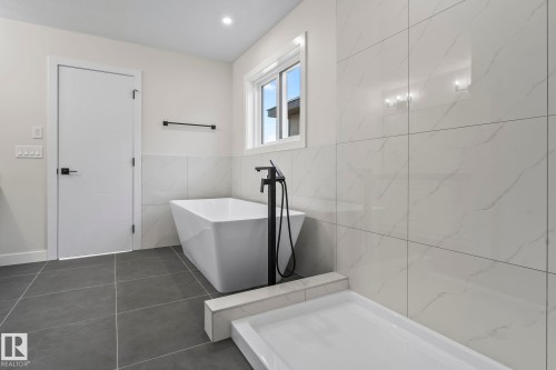 Contemporary bathroom featuring a freestanding tub with a matte black floor-mounted faucet, large format tile flooring, and a walk-in shower base - 208 Falcon Crescent, Leduc, AB - Indoor Photo Showing Bathroom