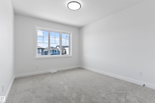 Bright room featuring a large window with grid pattern, light gray carpeting, white walls, and a modern flush-mount ceiling light - 208 Falcon Crescent, Leduc, AB - Indoor Photo Showing Other Room