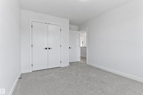Room featuring a neutral color palette, grey carpet flooring, white baseboards, and a pair of white bi-fold doors with matte black hardware - 208 Falcon Crescent, Leduc, AB - Indoor Photo Showing Other Room