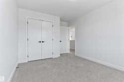 Room featuring a neutral color palette, grey carpet flooring, white baseboards, and a pair of white bi-fold doors with matte black hardware - 