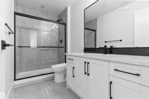 Modern bathroom featuring a glass-enclosed shower with matte black framing, large format gray tile flooring, a white vanity with black hardware, a rectangular mirror, and a sleek black faucet - 208 Falcon Crescent, Leduc, AB - Indoor Photo Showing Bathroom