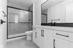 Modern bathroom featuring a glass-enclosed shower with matte black framing, large format gray tile flooring, a white vanity with black hardware, a rectangular mirror, and a sleek black faucet - 