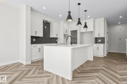 Kitchen featuring a white island, white cabinetry, dark subway tile backsplash, recessed lighting, and wood-finish herringbone flooring - 