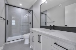 Contemporary bathroom featuring a spacious white vanity with ample storage, a light-toned countertop, and modern black hardware - 