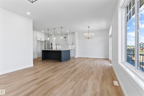 Open-concept main living area featuring wood-finish flooring, a contemporary kitchen island with pendant lighting, white cabinetry, recessed lighting, and a brass chandelier - 208 Falcon Crescent, Leduc, AB - Indoor