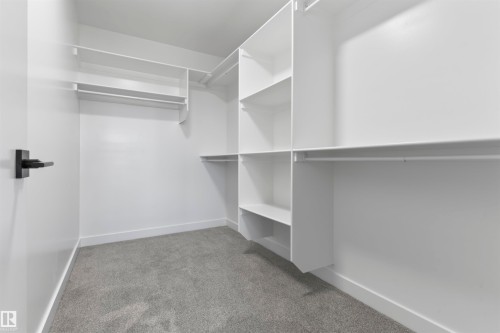 Walk-in closet featuring built-in white shelving, multiple hanging rods, white walls, white baseboards, and gray carpeting - 208 Falcon Crescent, Leduc, AB - Indoor With Storage