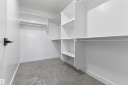 Walk-in closet featuring built-in white shelving, multiple hanging rods, white walls, white baseboards, and gray carpeting - 