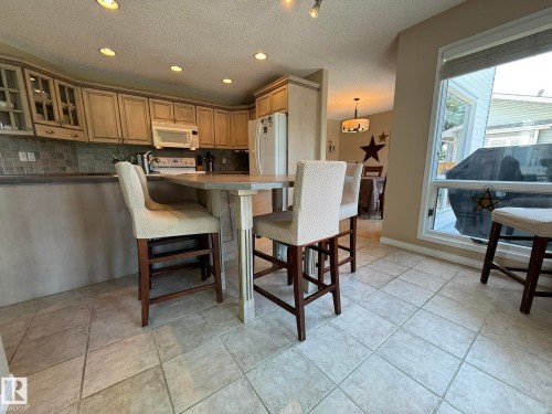 Kitchen featuring recessed lighting, light-toned cabinetry, tile flooring, a built-in breakfast bar, and a large window - 5604 57 Avenue, Beaumont, AB 