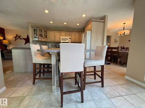 Kitchen featuring recessed lighting, a stone-finish countertop island with seating, upper and lower cabinetry, and a tile backsplash - 5604 57 Avenue, Beaumont, AB 