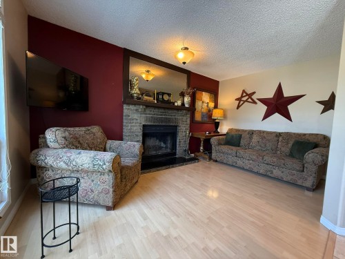 Living area featuring a brick-surround fireplace with a wood mantel, light wood-finish flooring, and a mounted ceiling light fixture - 5604 57 Avenue, Beaumont, AB 
