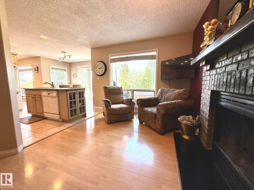 Living area featuring a brick fireplace with a dark hearth, wood-finish flooring, and expansive windows - 5604 57 Avenue, Beaumont, AB 