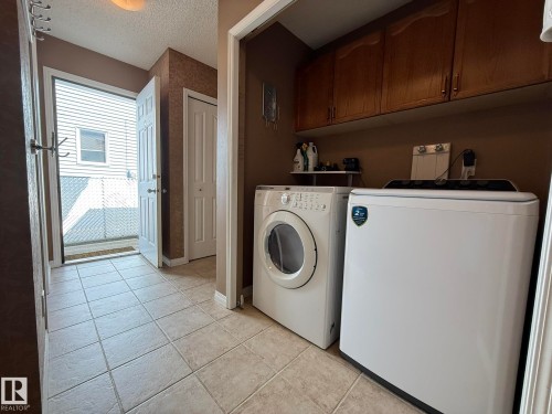 Dedicated laundry area featuring upper wood cabinetry and a neutral tile floor - 5604 57 Avenue, Beaumont, AB 