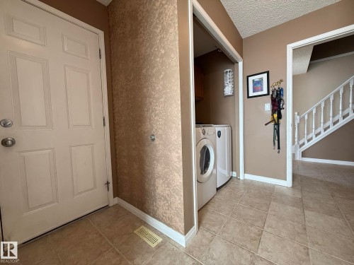 Dedicated laundry area with stacked appliances, featuring a front-loading washer and dryer - 5604 57 Avenue, Beaumont, AB 