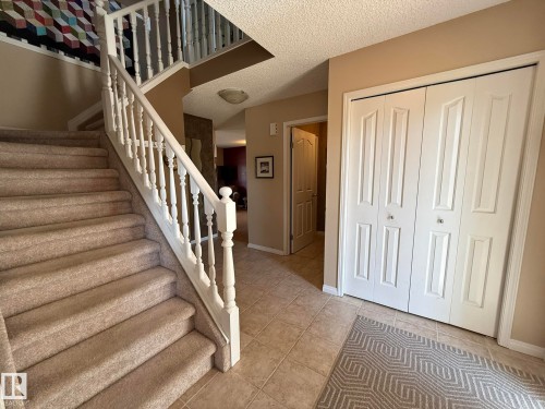 Inviting entry with tile flooring, a carpeted staircase featuring white balusters, and a double bi-fold closet - 5604 57 Avenue, Beaumont, AB 